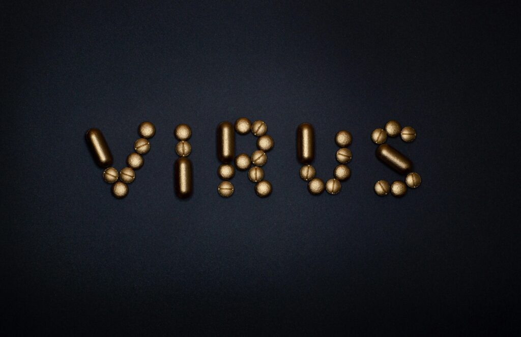 Golden pills arranged spelling 'virus' on a dark surface, symbolizing health themes.