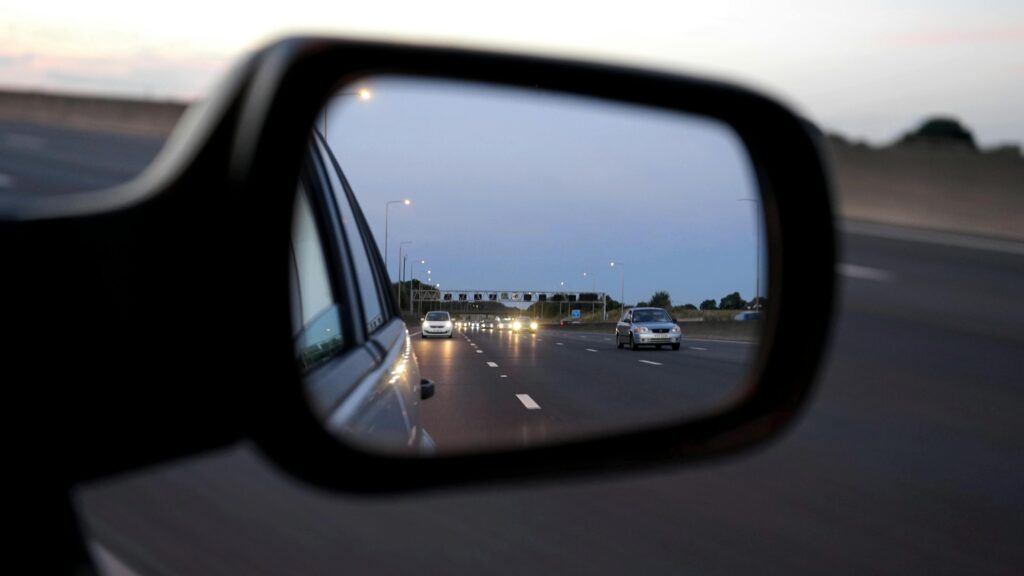 View of cars on the highway reflected in a vehicle's side mirror at twilight, capturing motion and speed.